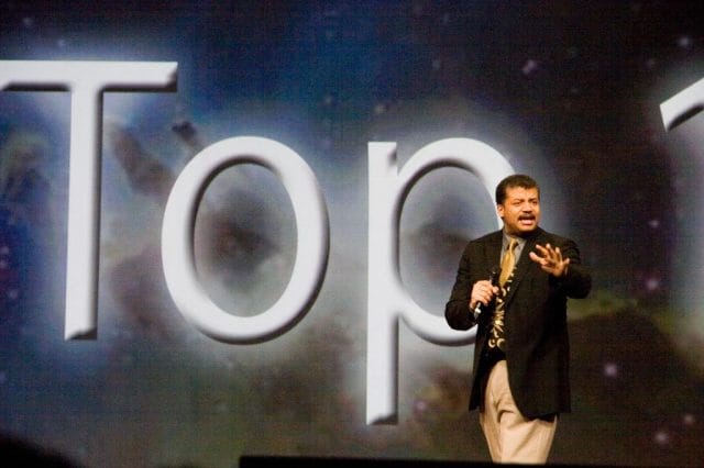 Neil deGrasse Tyson standing in front of a large logo