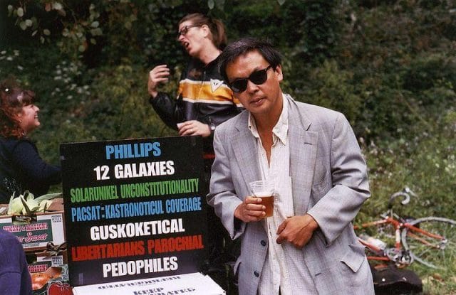 Frank Chu holding a glass and standing next to a sign