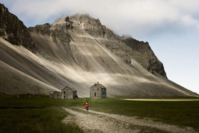 a person walking on a dirt road in front of a house on a mountain