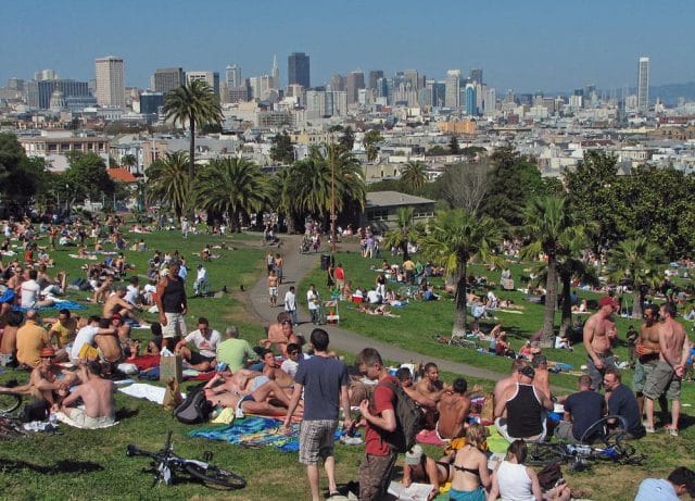 a group of people sitting on the grass in front of Mission Dolores Park