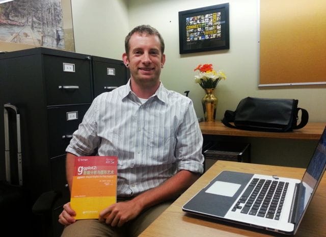 Hadley Wickham sitting at a desk with a laptop and a box