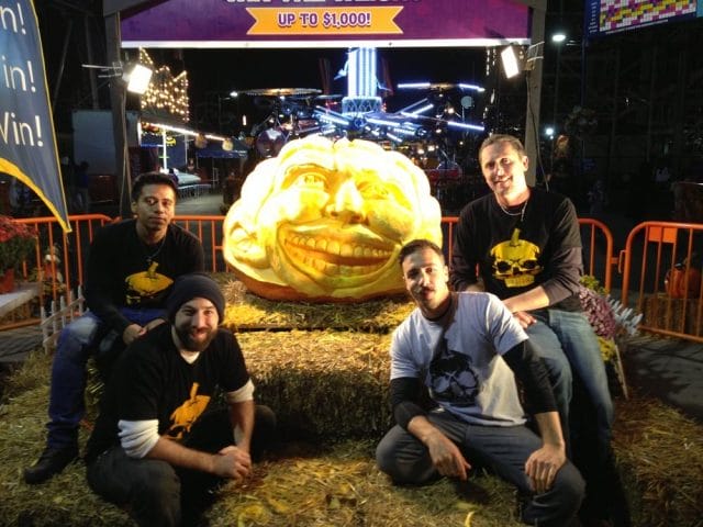 a group of men posing for a picture next to a large pumpkin