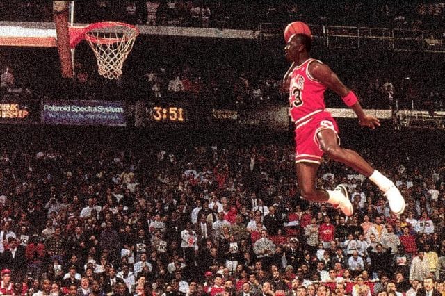 a man jumping in the air with a basketball in front of a crowd