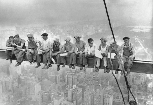 a group of men sitting on a metal railing above a city