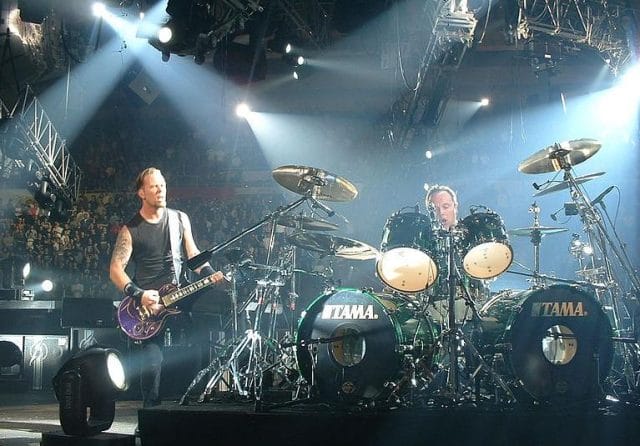 a person playing a guitar on a stage with a drum set and a crowd of people