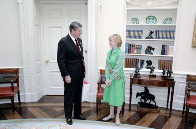 a man and a woman standing in a room with a bookcase
