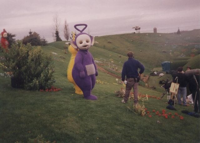 a person in a garment walking on a grass hill with people and flowers