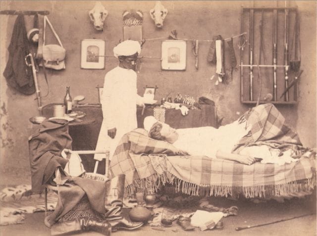 a person in a white robe in a room with a bed and a person in a white hat