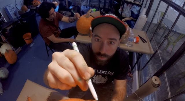 a person with a beard and a hat sitting at a table with a drink and a glass with