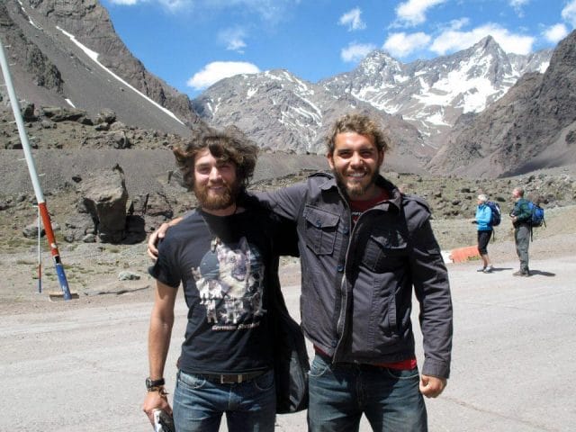 two men standing on a rocky path with snow covered mountains in the background