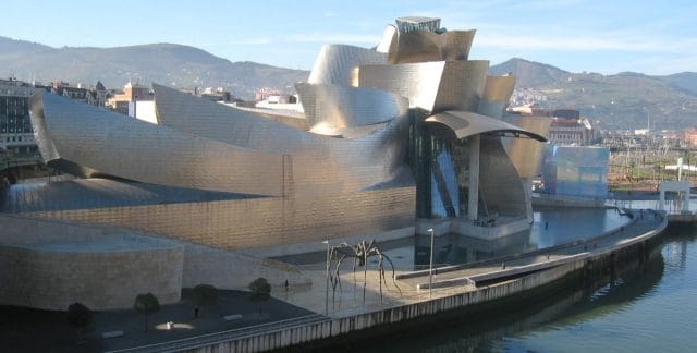 a large building with a curved roof with Guggenheim Museum Bilbao in the background