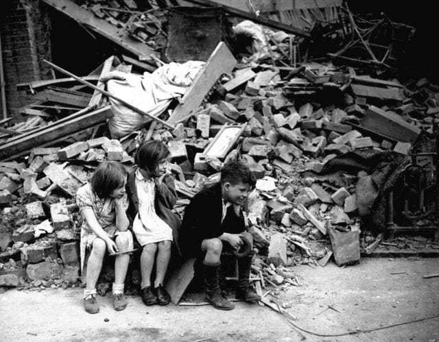 a group of children sitting on the ground next to a pile of rubble