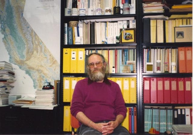 Jon Postel sitting in a chair in front of a book shelf