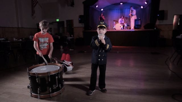 a person singing into a microphone next to a boy playing drums