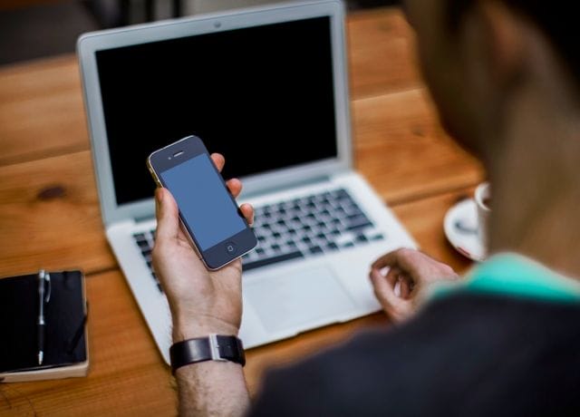 a person holding a cell phone and a laptop