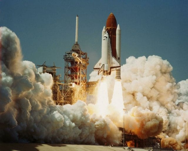 a space shuttle launching off with Kennedy Space Center in the background