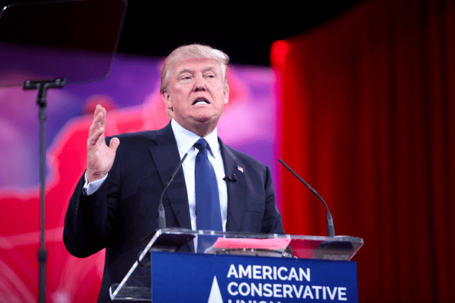 Donald Trump standing at a podium with a microphone and a sign