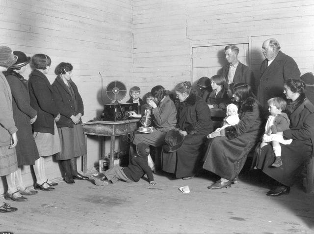 a group of people standing around a man sitting on a chair