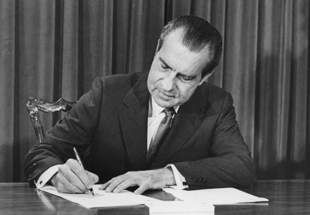 Richard Nixon sitting at a desk writing on a book