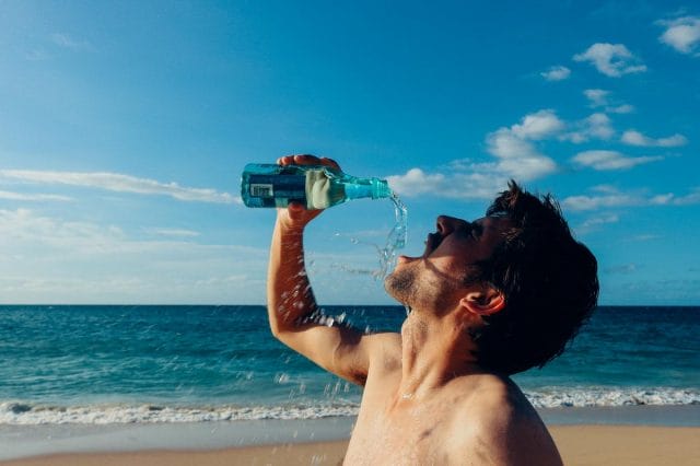 a person drinking from a bottle on a beach