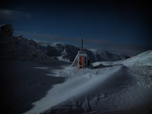 a small white building on a snowy mountain